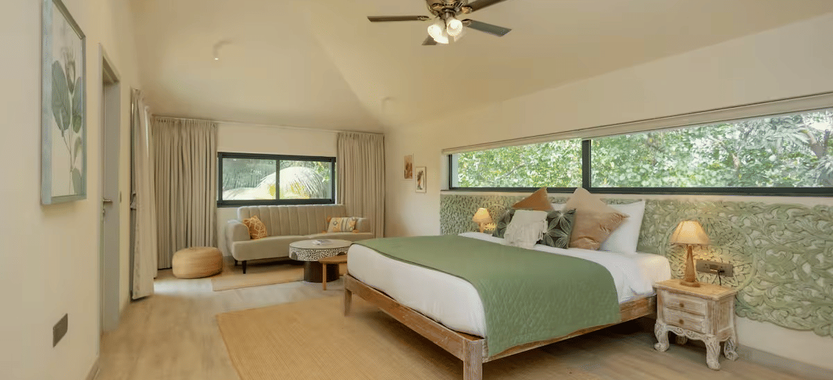 Diagonal view of the room with a large bed, bedside tables with lamps on both sides, rectangular window panels, and natural light at Lime Tree Villa with Private Pool | Luxury Stay in Goa.